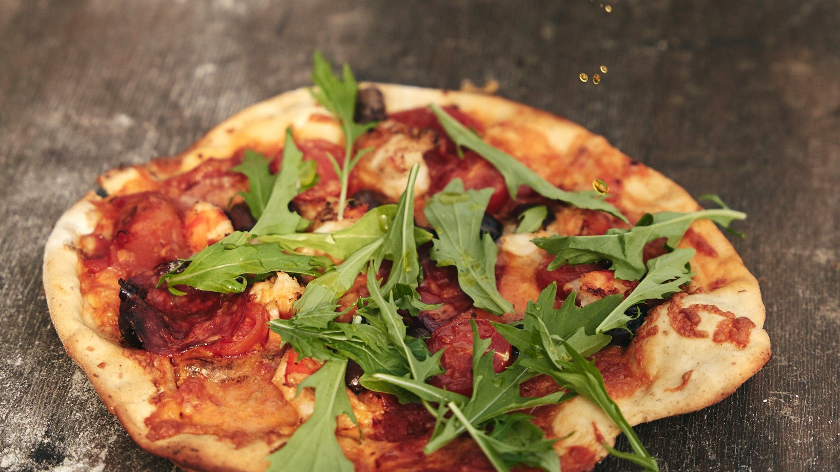 Pizza with leopard-spotted crust baking on a pizza stone inside a Bastard kamado