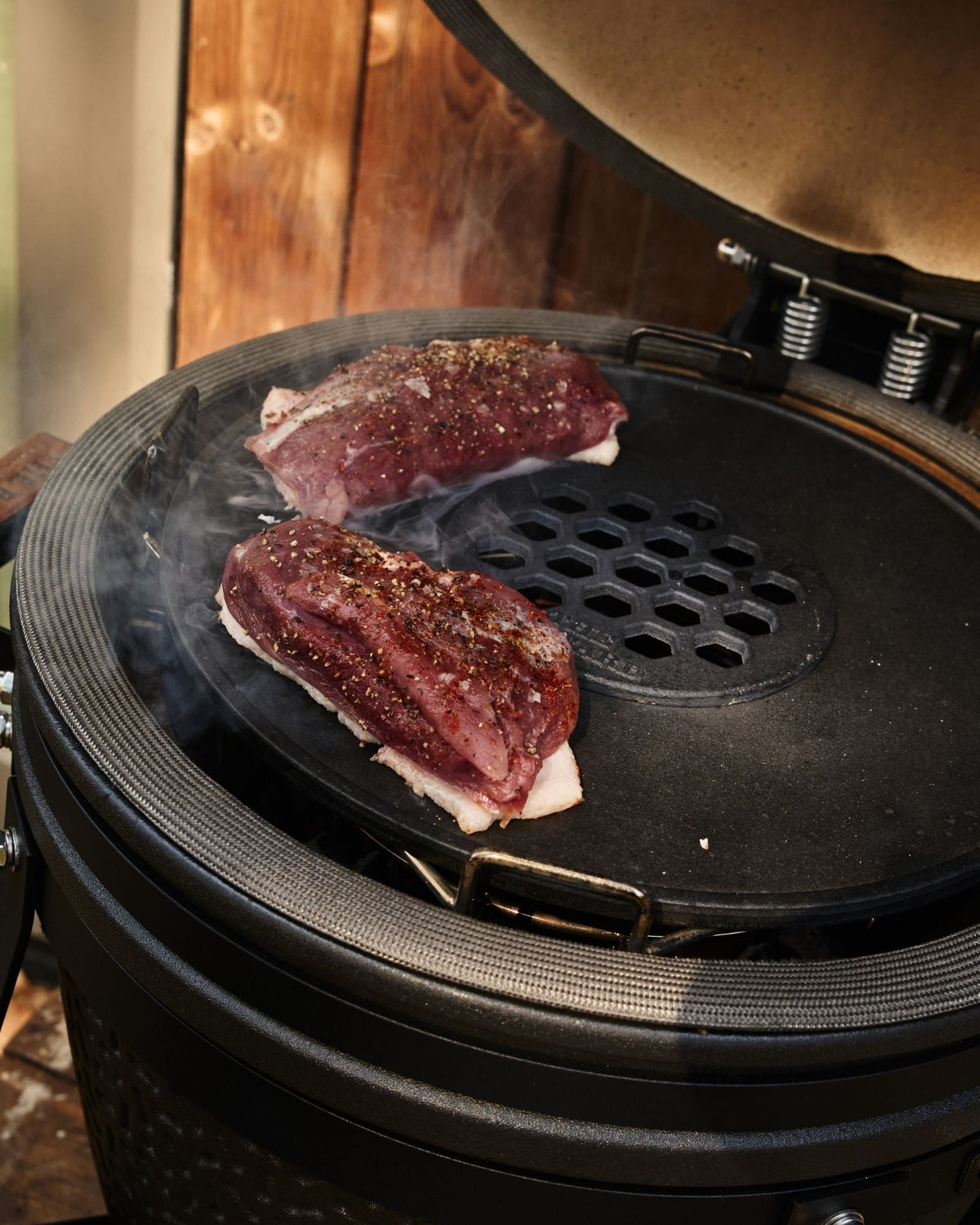 Two seasoned duck breast fillets searing skin-side down on the Plancha Ring on a Bastard kamado, with smoke rising