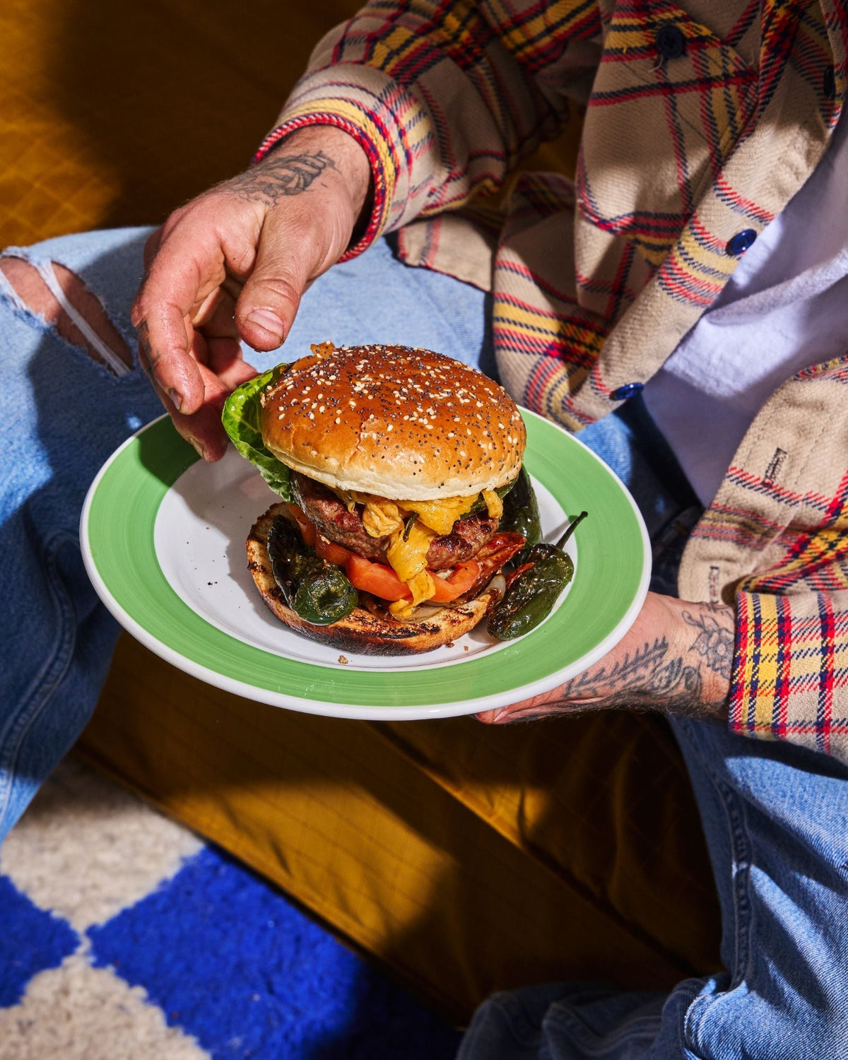 Cheeseburger with melted cheese, tomato and grilled padrón peppers and jalapeños on a green-rimmed plate