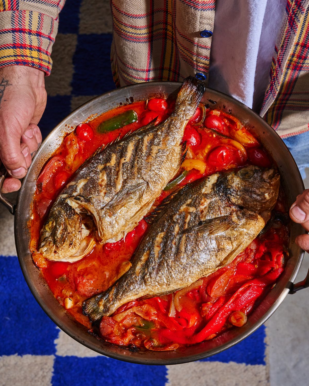 Two grilled sea bream on a bed of roasted pepper and tomato sauce in a large pan