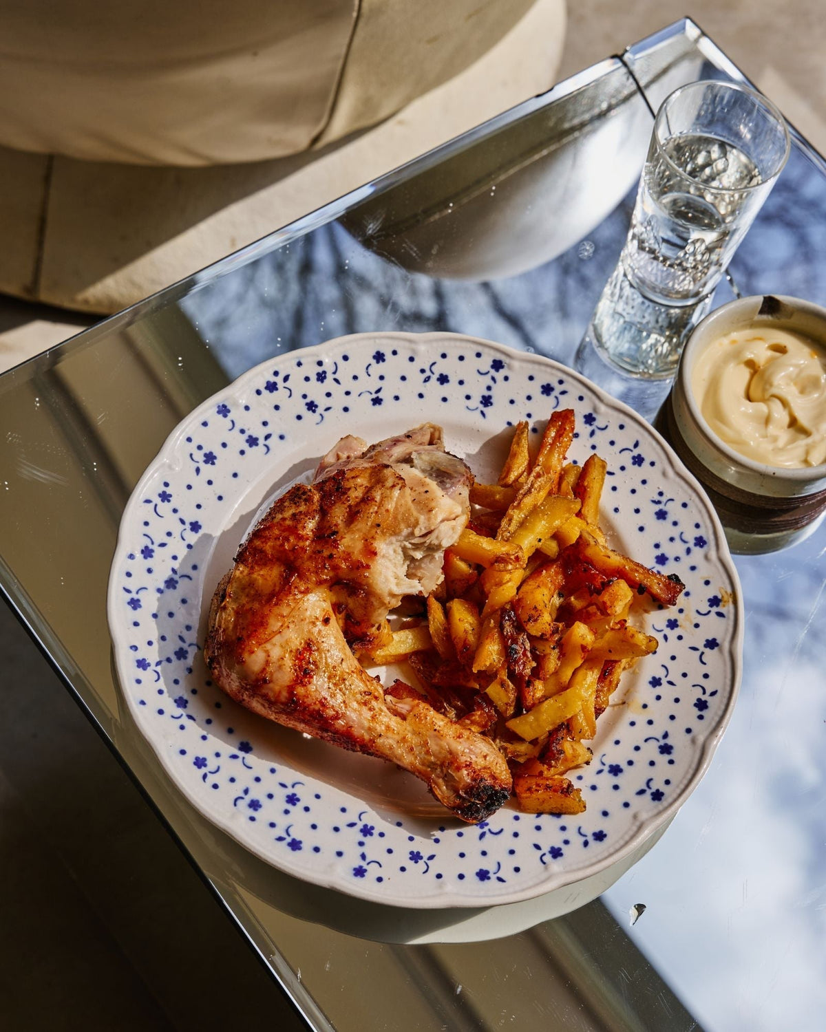 Smoked chicken leg quarter with chunky fries and a pot of aioli on a blue patterned plate
